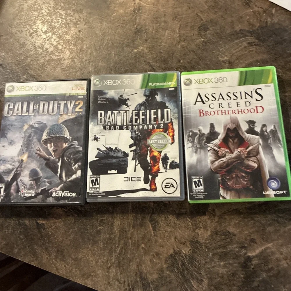 Three Xbox 360 Games, Assassin Creed, Battlefield, And Call Of Duty
